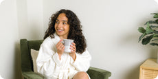Image of a woman in a Featherweight Robe, sitting in a green chair, drinking coffee