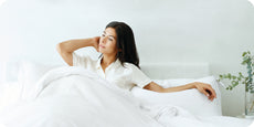 Image of a woman sitting up in bed surrounded by all white bedding