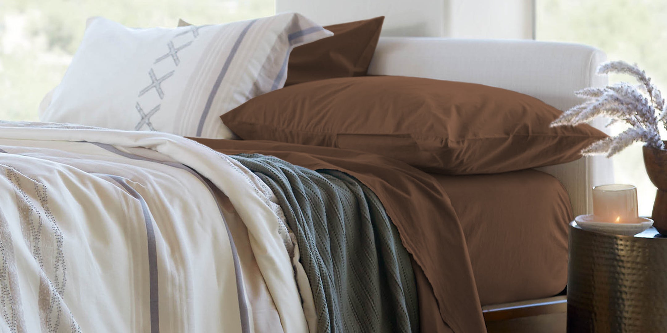 Image of a bed with cacao Blended Linen sheets, agave Ridgeback Coverlet, and Sonoran Duvet Cover in a room with plenty of natural light