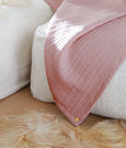 Image of an Ash Rose Everyday Cotton Coverlet draped over a white pouf