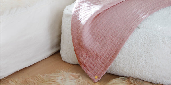 Image of an Ash Rose Everyday Cotton Coverlet draped over a white pouf
