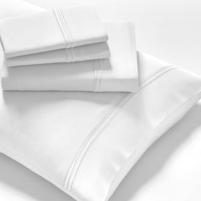 Image showcasing entire White Refreshing TENCEL™ Lyocell Sheet Set. The image includes: a fitted sheet on the bed, a pillowcase on a pillow, a neatly folded flat sheet, and two neatly folded pillowcases.
