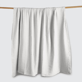 Image of a Bright White Everyday Cotton Coverlet hanging and draped over a wooden rod on a white background