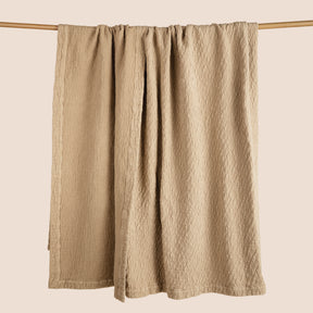 Image of an Ochre Wave Coverlet hanging and draped over a wooden rod on a light pink background