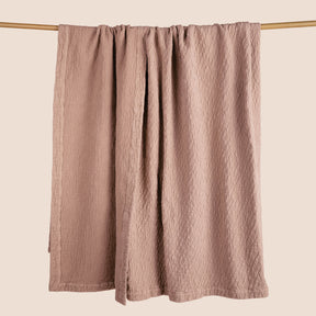 Image of a Pink Sandstone Wave Coverlet hanging and draped over a wooden rod on a light pink background