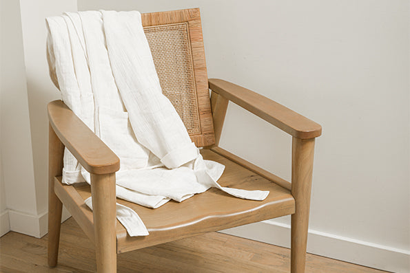 Image of a white Featherweight Robe draped over a tan wooden chair in the corner of a room