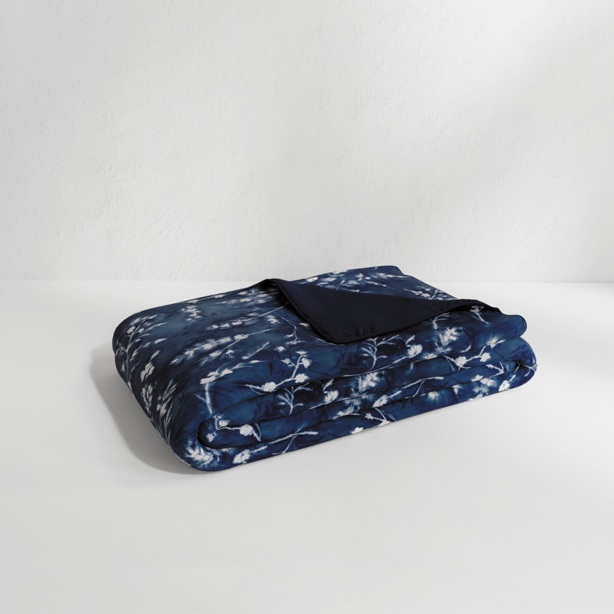 Image of the Floral Midnight Duvet Cover + Cooling neatly folded with the floral side facing up and the back right corner folded over to show the reversible plain Midnight side