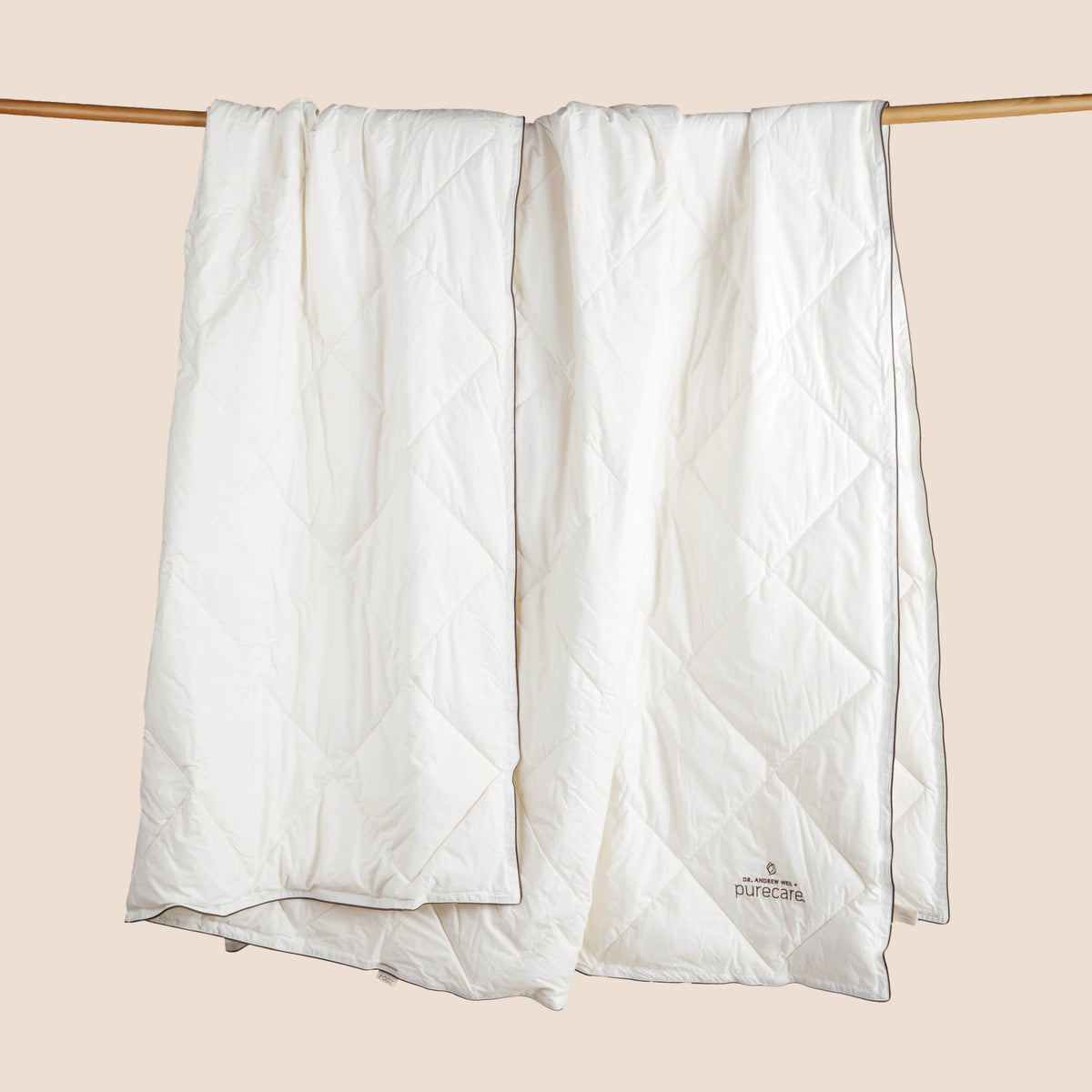 Image of an off-white All Seasons Wool Duvet Insert hanging and draped over a wooden rod on a light pink background