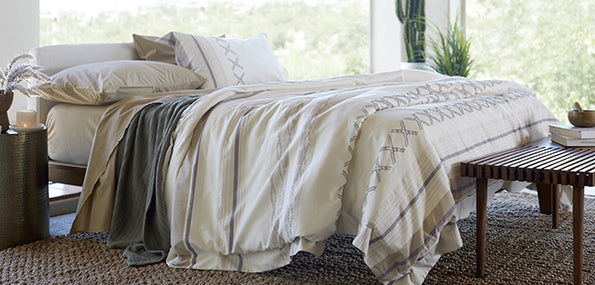 Image of a made bed with a large window behind it. The bed showcases Ochre Garment Washed Percale Sheets, an Agave Ridgeback Coverlet, and a Sonoran Duvet Cover.