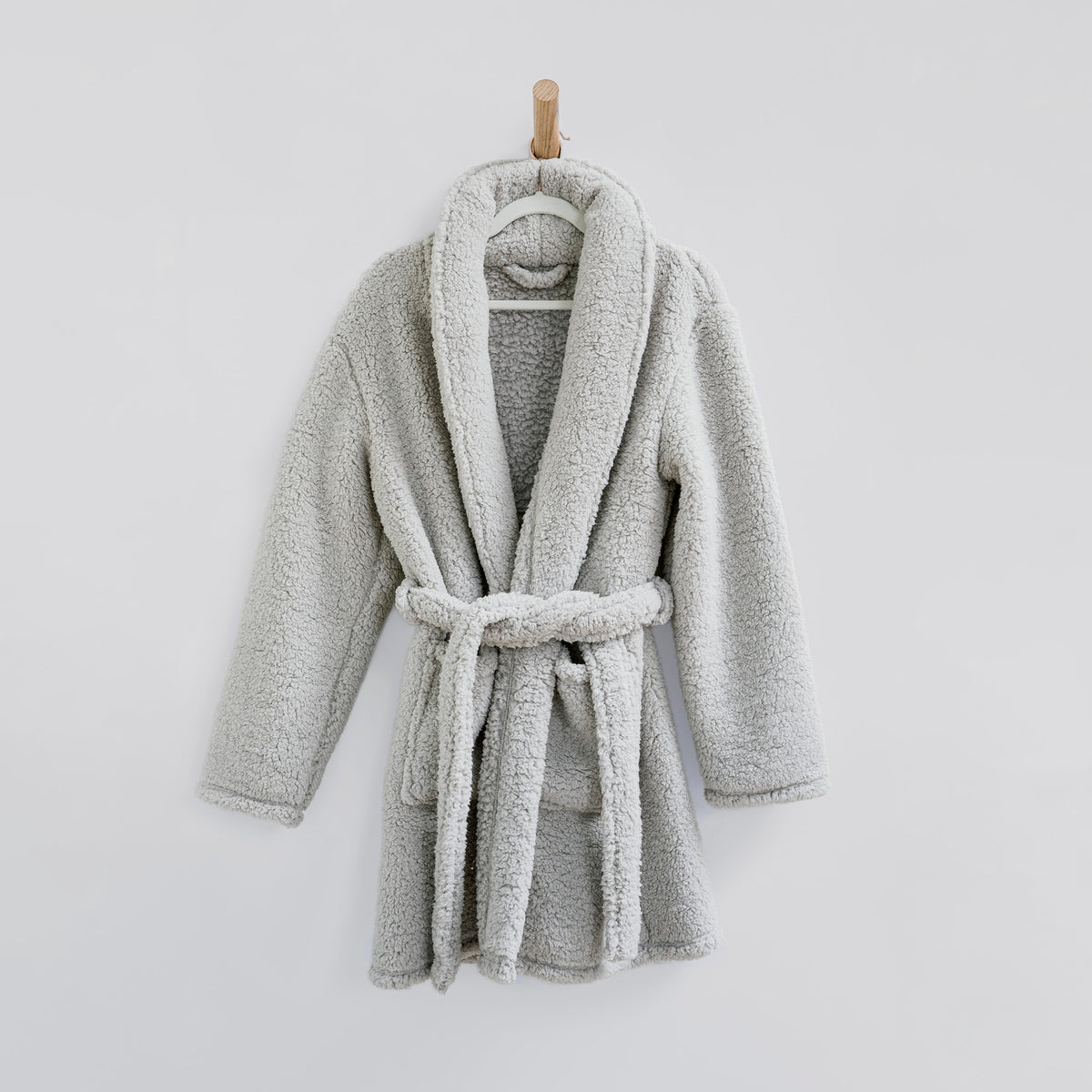Image of a fluffy gray Sunday Morning Robe hanging from a wooden rod on a white wall