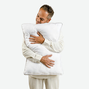 Image of a man facing forward with his head leaning against the Cooling Fiber Pillow he's hugging towards him 