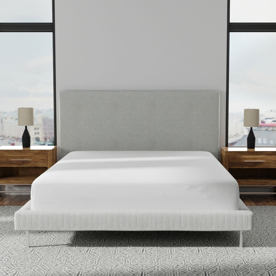 Image of a bedroom with a bed in the middle of the room with just a white mattress protector on it