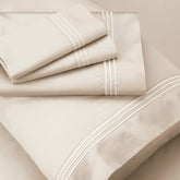 Image of Ivory Recovery Cotton Shed Set shown top to bottom with two folded pillowcases, one flat sheet, a pillowcase shown on a pillow, and a fitted sheet underneath