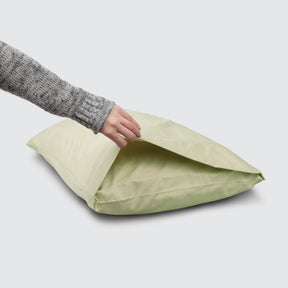 Image of a Sage Bamboo Rayon Pillowcase on a pillow with a hand lifting up the edge to showcase the enveloping design