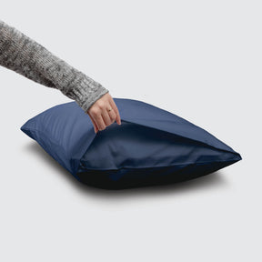 Image of a Celestial Blue Refreshing TENCEL™ Lyocell Pillowcase on a pillow with a hand lifting up the edge to showcase the enveloping design