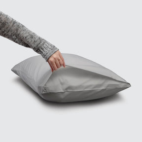 Image of a Dove Gray Refreshing TENCEL™ Lyocell Pillowcase on a pillow with a hand lifting up the edge to showcase the enveloping design