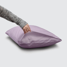 Image of a Lilac Refreshing TENCEL™ Lyocell Pillowcase on a pillow with a hand lifting up the edge to showcase the enveloping design