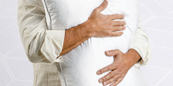 Image of a man hugging a Cooling Shattered Ice Pillow against his chest. The background of the image is a close-up of the snowflake design on the cover of the pillow