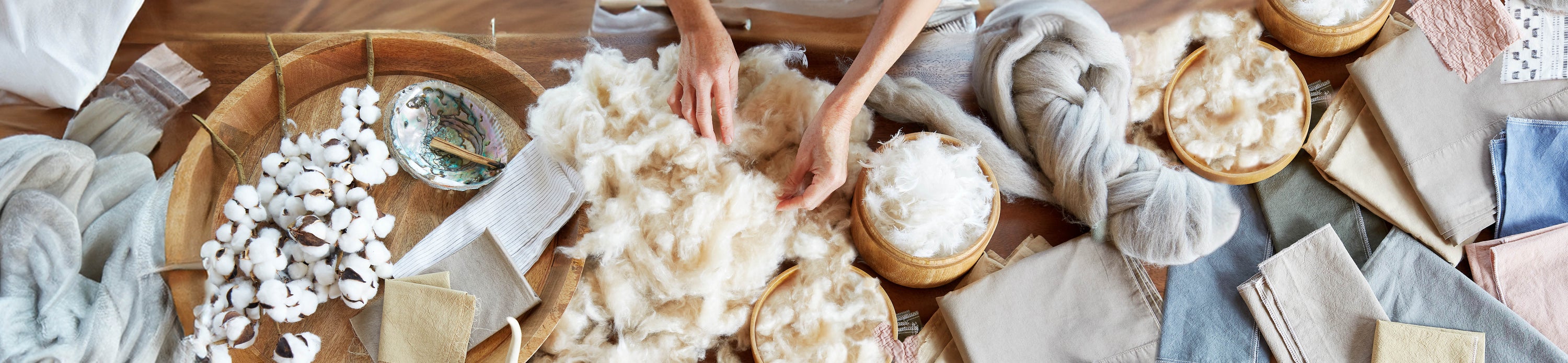 Image of two hands feeling wool on a table of various other fabrics and materials
