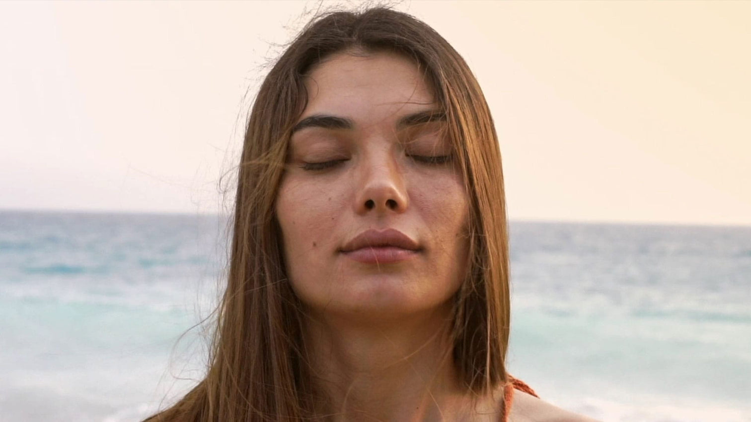 Image of a woman standing by an ocean with her eyes closed