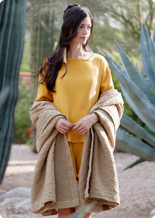 Image of a woman dressed in yellow and standing outside with the Ochre Dr. Weil Wave Coverlet wrapped around her