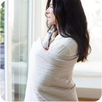 Image of a woman staring out her window and wrapped in the Ecru Dr. Weil Ridgeback Coverlet