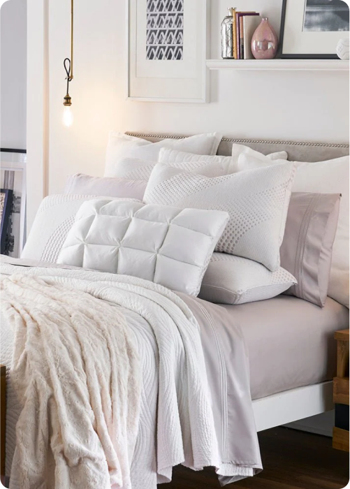Image of a white/neutral colored bed with nine different pillows of various sizes and types showcased at the head of the bed