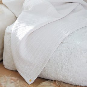 Image of the Bright White Everyday Cotton Coverlet draped over a fluffy white pouf 