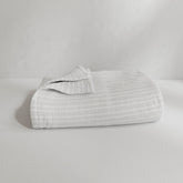 Image of a neatly folded Bright White Everyday Cotton Coverlet with the back left corner folded up on a white background