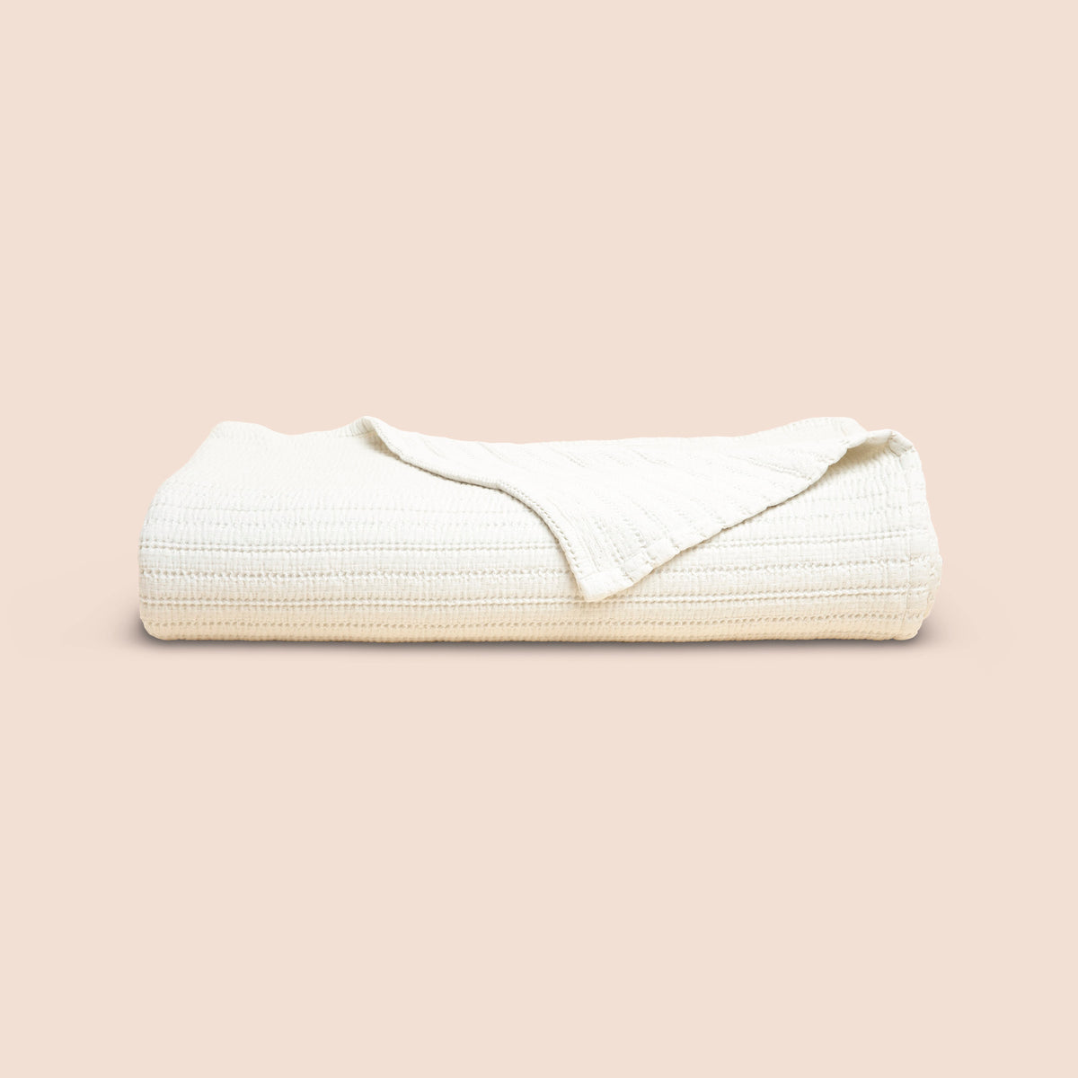 Image of Ecru Ridgeback Coverlet neatly folded with one corner folded forward on a light pink background