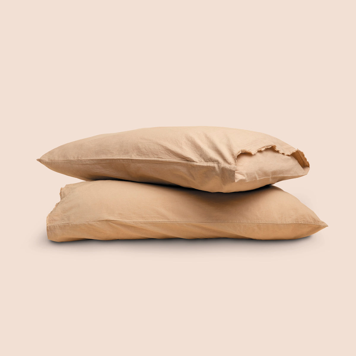 Image of two pillows with Ochre Garment Washed Percale pillowcases stacked on top of each other on a light pink background. The top pillow is showcasing an enveloping feature. 