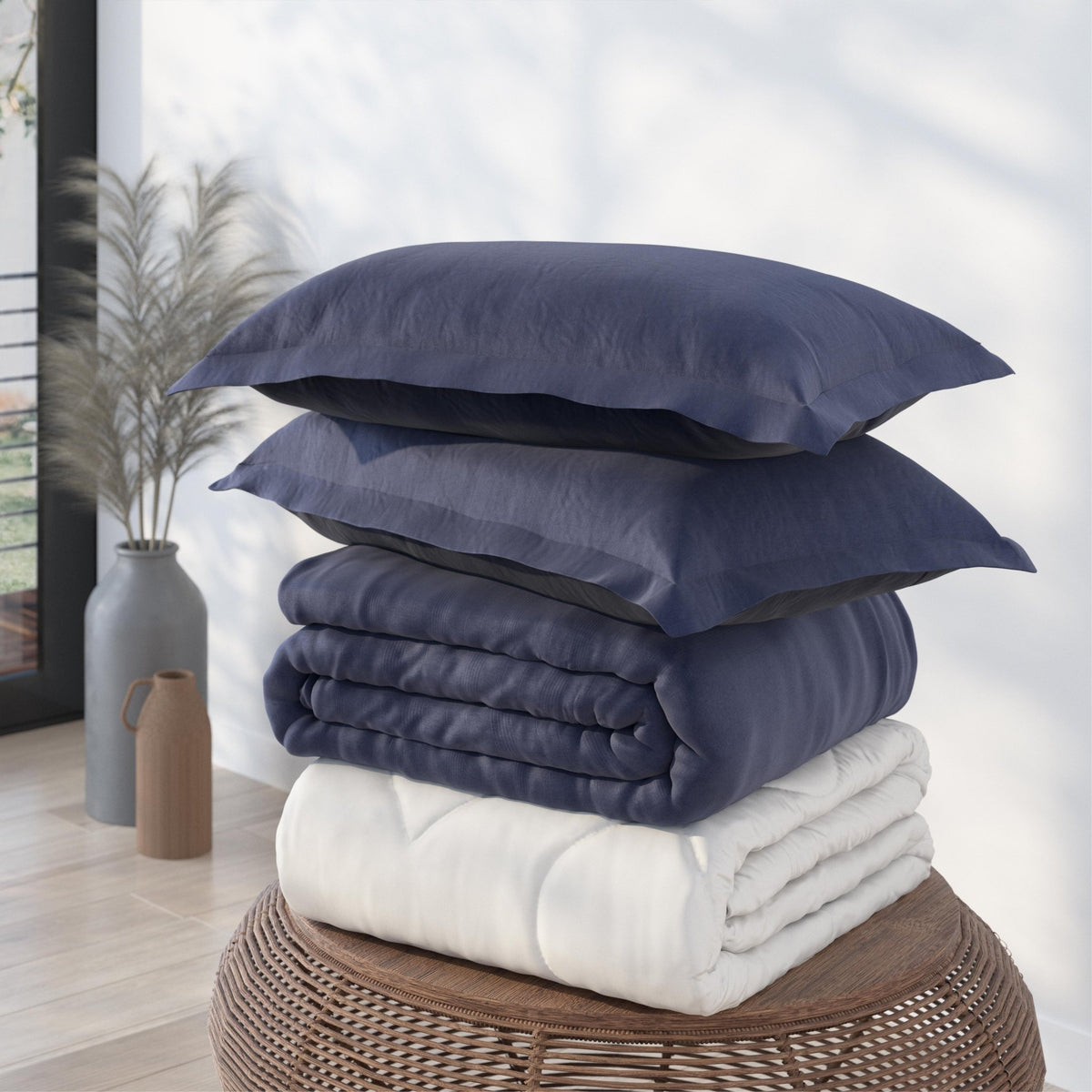 Image of a pile of bedding on top of a brown table. The bedding shown includes (from top to bottom): 2 Midnight/Celestial Pillow Shams with the Midnight side facing up, a neatly folded Midnight/Celestial Duvet Cover + Cooling with the Midnight side showing, and a neatly folded Cooling Duvet Insert 